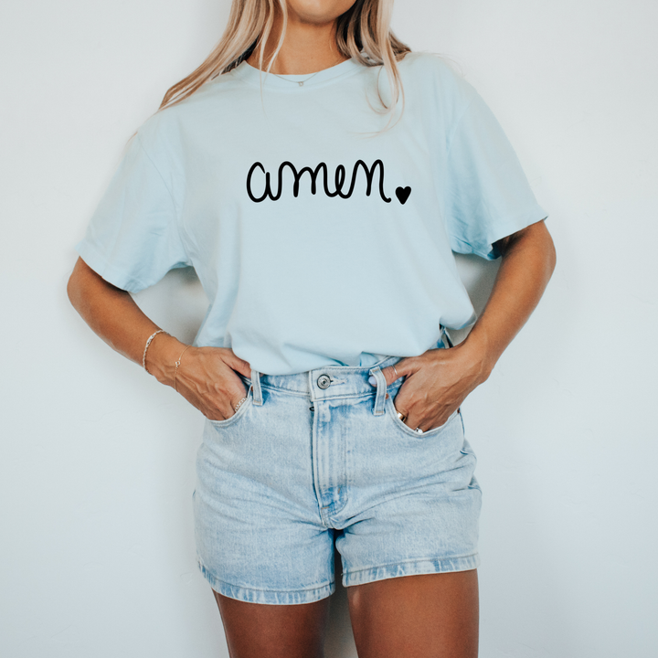 Person wearing a light blue t-shirt with 'amen' printed on it and denim shorts against a white background