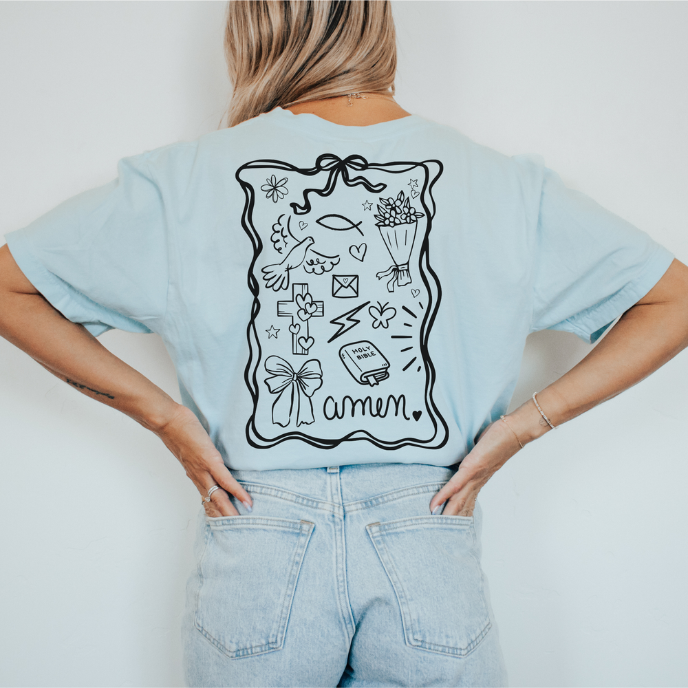 Person wearing a light blue t-shirt with a graphic design on the back, sitting on a white surface.