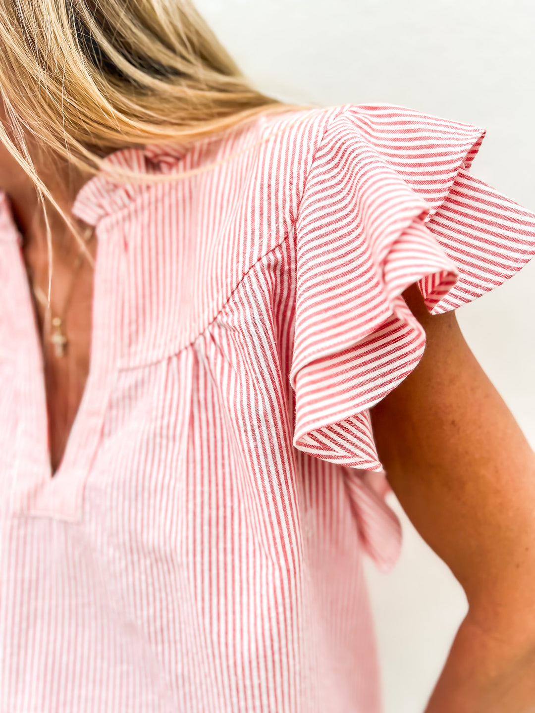 Woman wearing a red and white striped flutter sleeve top with a ruffle detail and notched neckline, styled with denim jeans, looking down and smiling