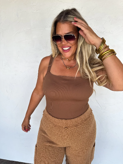 Woman wearing a brown outfit with sunglasses against a white background