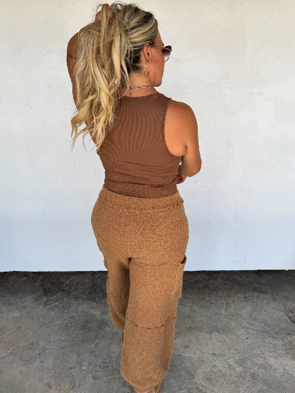 Woman wearing a brown ribbed outfit standing against a white wall.