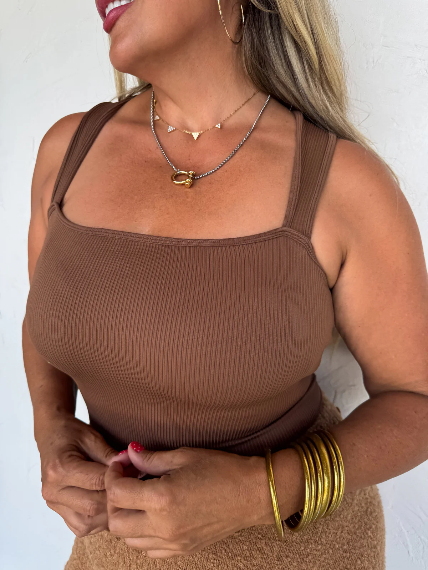 Woman wearing a brown tank top with gold jewelry against a white background