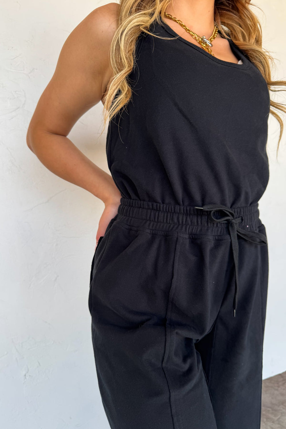 Person wearing a black sleeveless jumpsuit against a white background