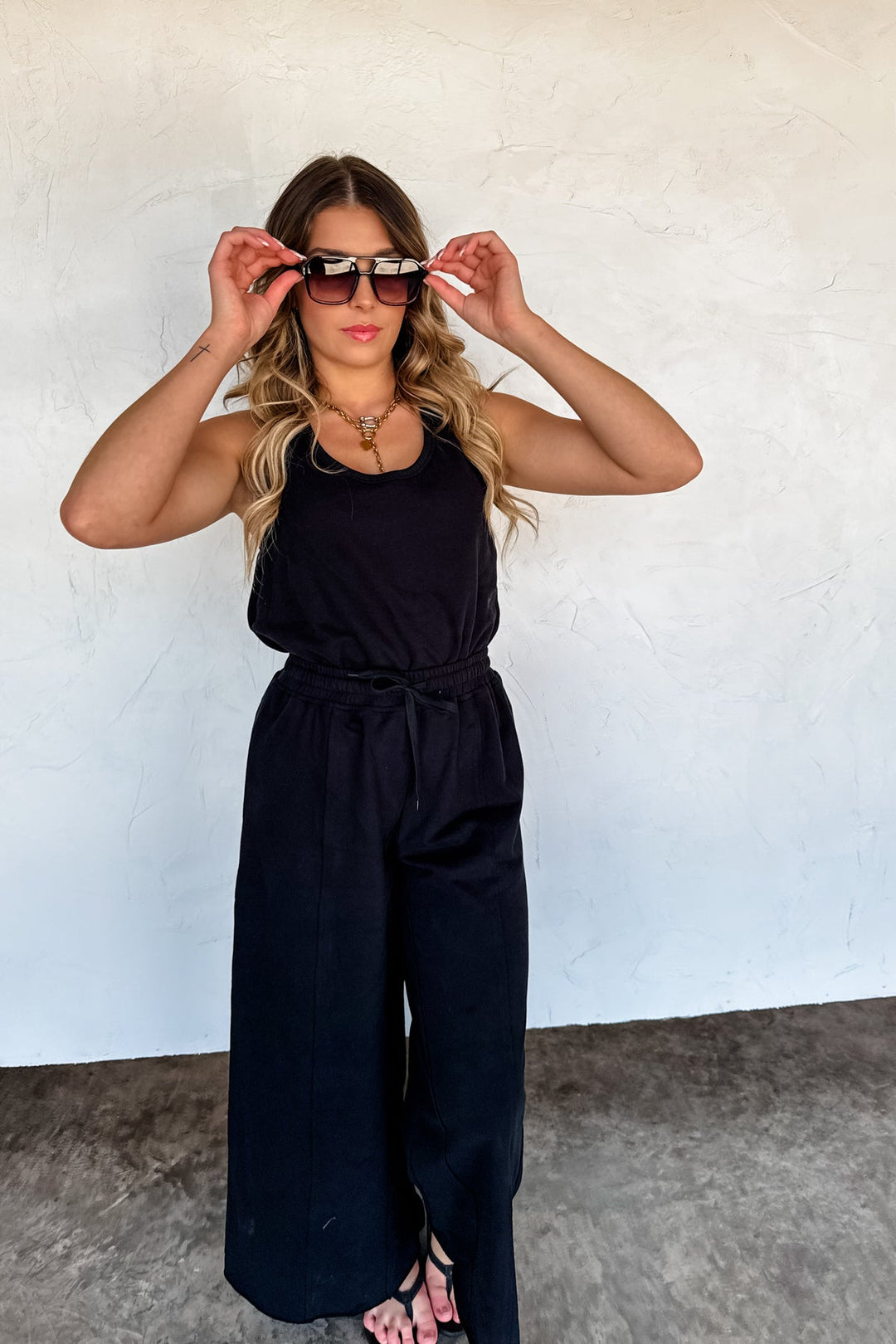Woman wearing a black jumpsuit against a white wall