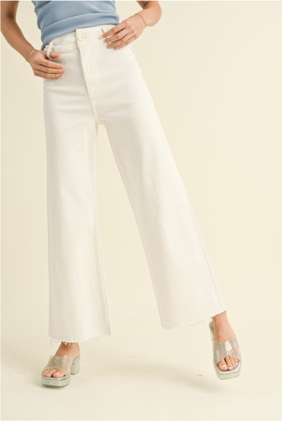 Woman wearing high-waisted white straight wide leg denim jeans with raw hem and platform sandals

