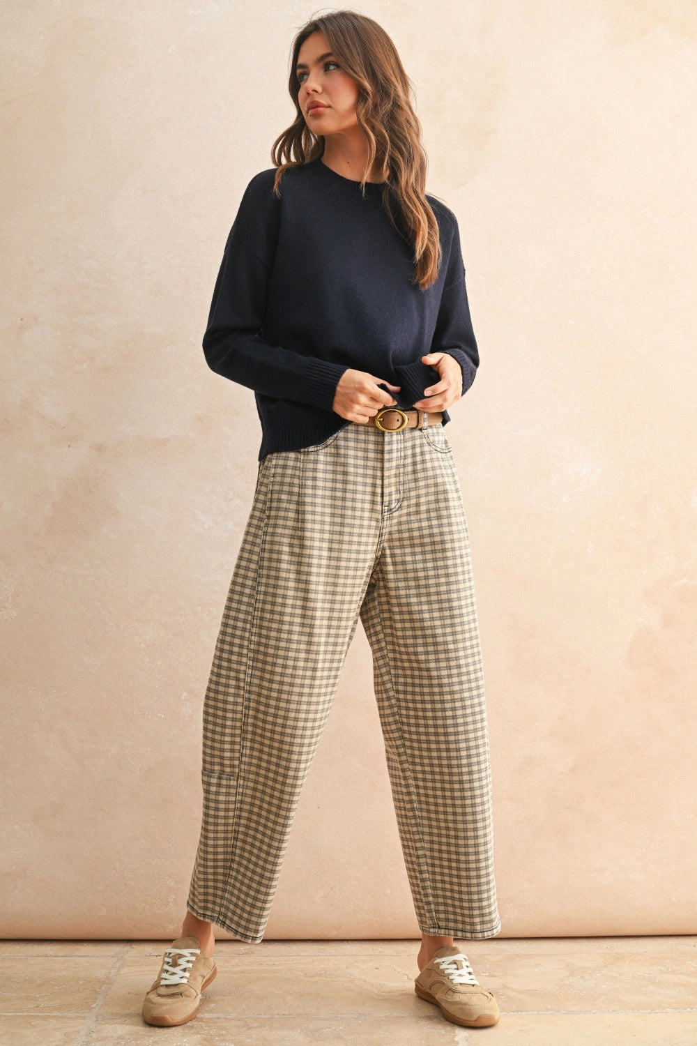 Woman wearing a navy sweater and plaid pants against a beige background